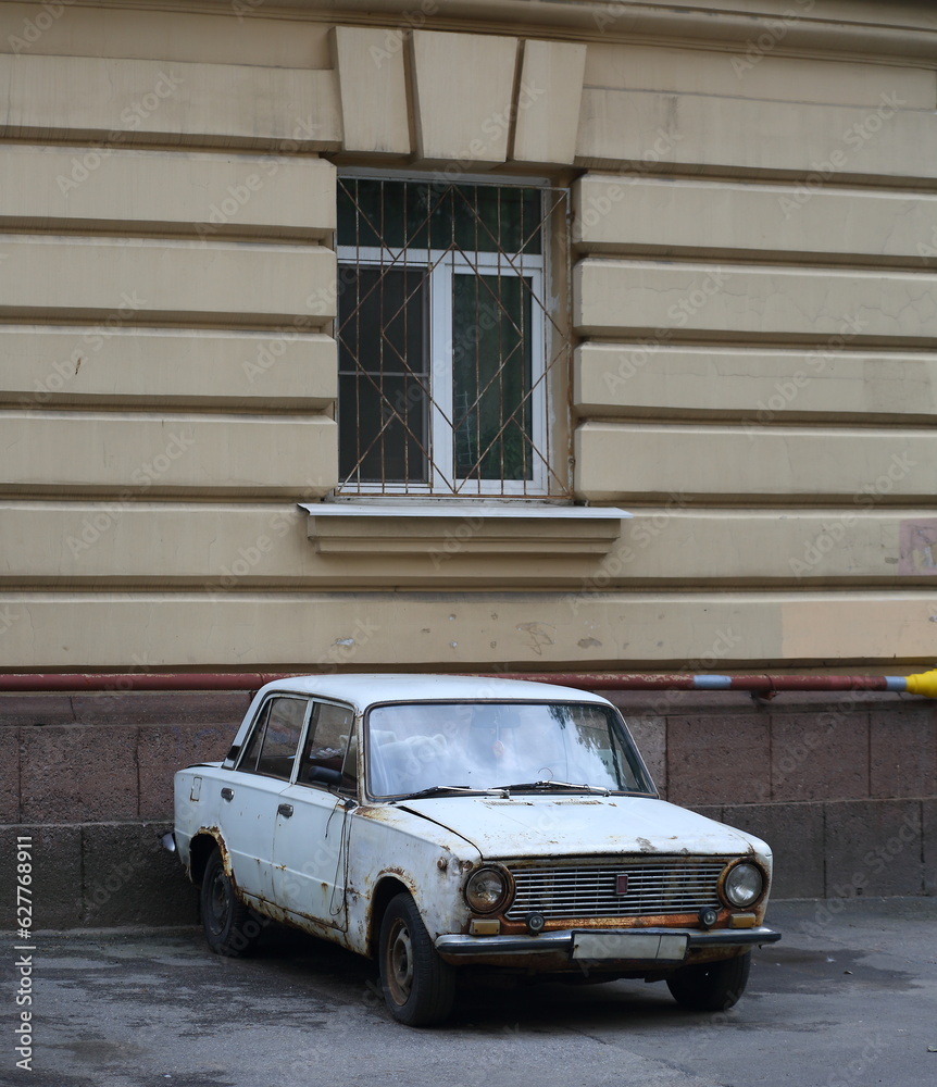 An old rusty white Soviet car stands under the window of a residential building, Sedova Street, Saint Petersburg, Russia, July 26, 2023