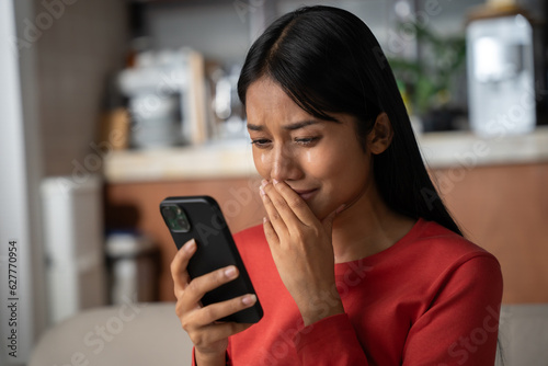 Beautiful asian woman looking to phone and crying. She was shocked with the bad news she received.