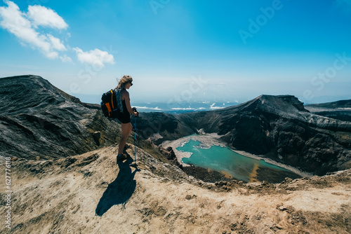 Woman with backpack and trekking poles standing on the mountain top above crater of Gorely volcano, Kamchatka photo