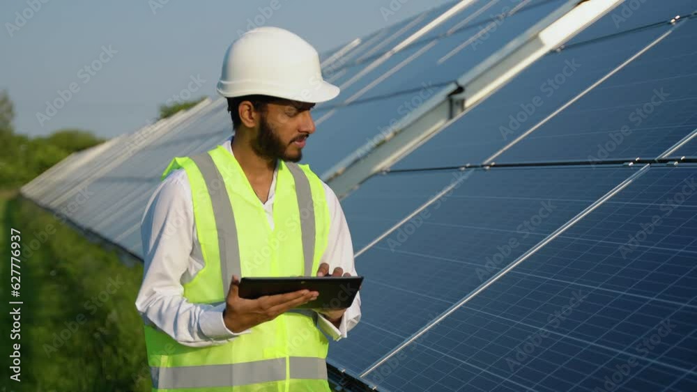 Young indian engineer working on tablet standing near solar panels with clear blue sky. Renewable green and clean energy. Copy space. Worker on job. Skill india