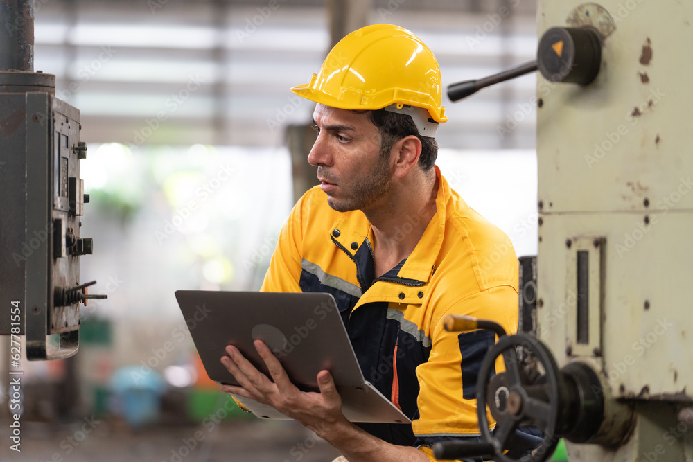 Caucasian male engineer in helmet working in industrial factory. Specialist engineer is using laptop and checking machine Caucasian male engineer in helmet working in industrial factory. Specialist engineer is using laptop and checking machine