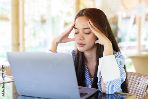 Free Download Asian woman with stressed back working in front of one laptop computer on front desk. with a stern expression, rubbing his head with his hands having a headache from work - GFXLoad