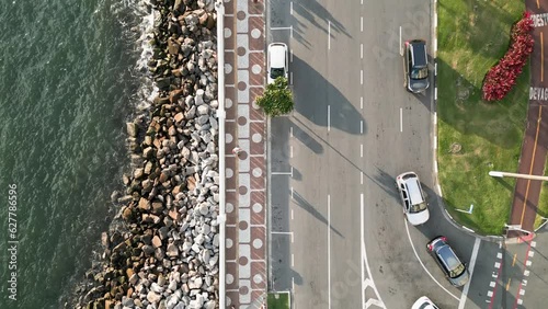 Aerial view from top to bottom of waves crashing on the rocks of the seaside avenue in Santos, Brazil. Cinematic video of the avenue coastline with people walking outdoors and cycling. 