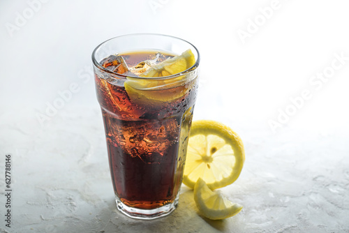 Fresh cola with ice cubes and lemon slices in a drinking glass, sweet caffeine drink against a light gray background, copy space, selected focus