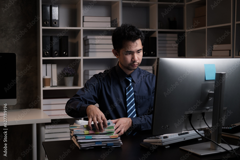 Tired young Asian businessman working overtime in the office room at night, trying to get things done before the deadline. Tired young Asian businessman working overtime in the office room at night, trying to get things done before the deadline.