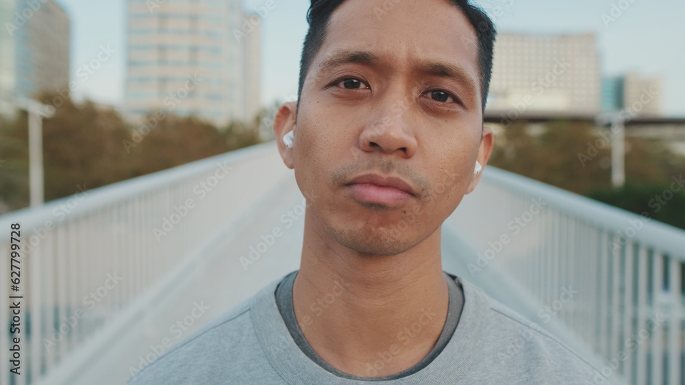 Close up, athlete in wireless headphones, a guy in sportswear, stands on a bridge and looks at the camera, listens to music Close up, athlete in wireless headphones, a guy in sportswear, stands on a bridge and looks at the camera, listens to music