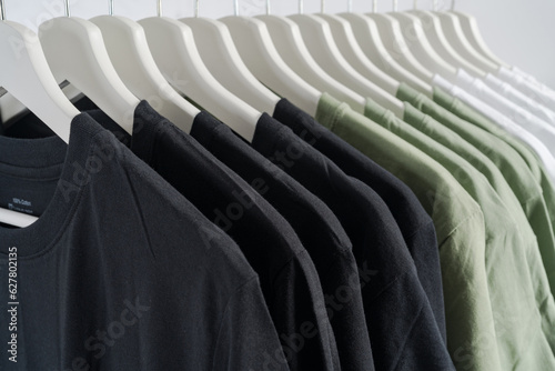 close up collection of black-white and green color t-shirt hanging on wooden clothes hanger