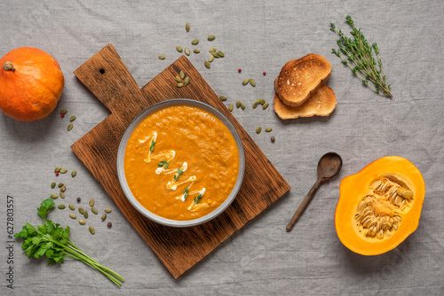 Pumpkin cream soup with toast on a gray linen tablecloth. Cozy thanksgiving dinner. Top view, flat lay.