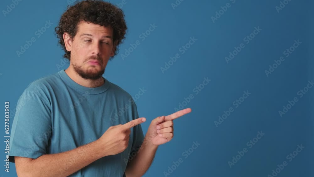 Surprised man pointing his fingers to show mockup space in studio isolated on blue background