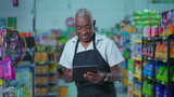 Happy Portrait of Brazilian Senior Supermarket Staff Holding Tablet, Joyful Older Male Employee in Apron