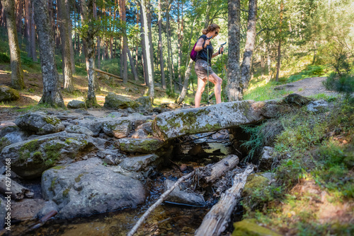 Senior woman hiking through a forest and crossing a stream with large stones, Madrid.