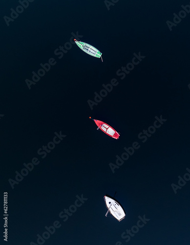 Topdown shot of three boats on a dark surface of a lake. 