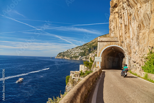 Fototapeta Naklejka Na Ścianę i Meble -  Scooter drives along the road along the Amalfi coast, approaching the tunnel Conca dei Marini
