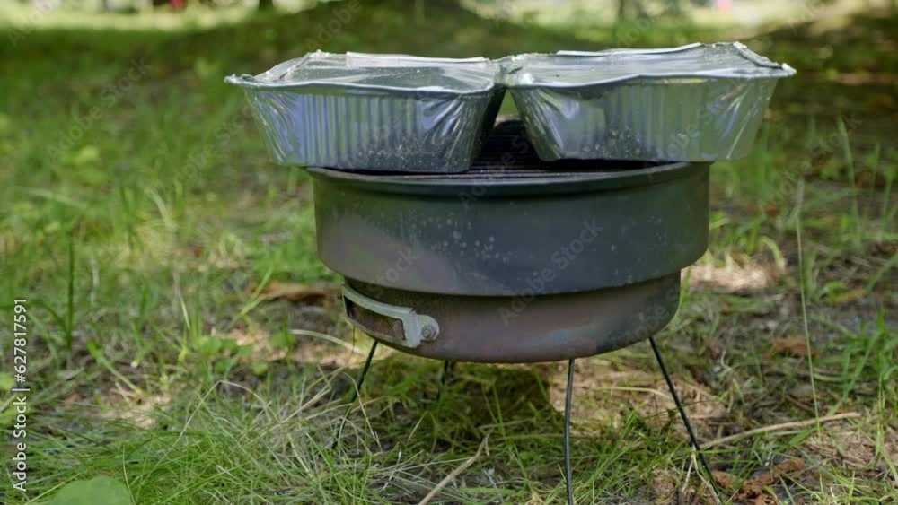 Old small rusty grill spread out on the grass in the park. The perfect outdoor grill. On the grill, 2 aluminum trays with food inside Old small rusty grill spread out on the grass in the park. The perfect outdoor grill. On the grill, 2 aluminum trays with food inside