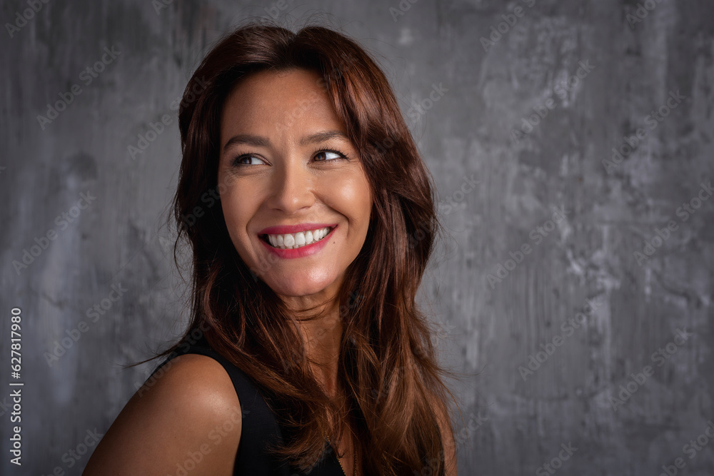 Close-up of a beautiful brown-haired woman standing in front of a grey wall and cheerful smiling