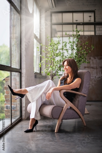 Full length of an attractive woman sitting in an armchair by the window