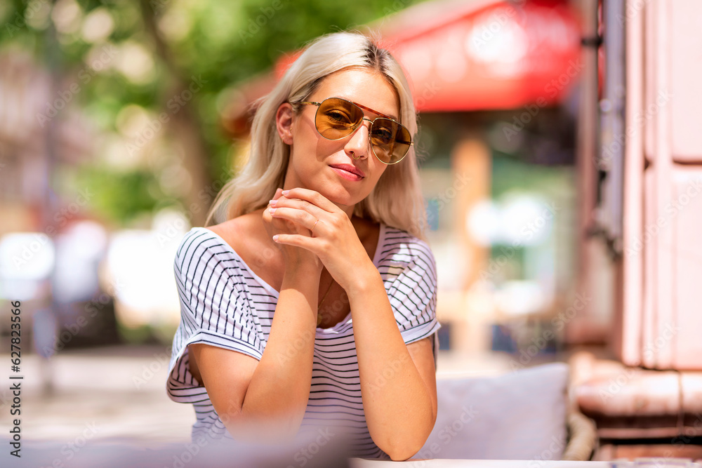 Portrait of a young girl with blonde hair and sunglasses is sitting outside