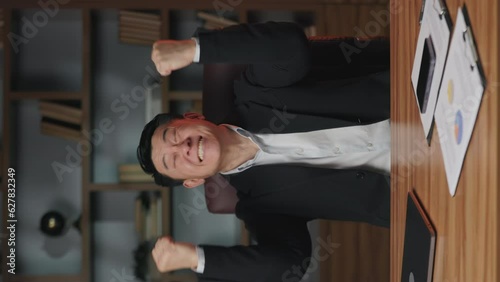 Close up view of emotional entrepreneur in business suit lifting fists in winner gesture while staying indoors. Vertical video of thrilled employer screaming in excitement while sitting in office.