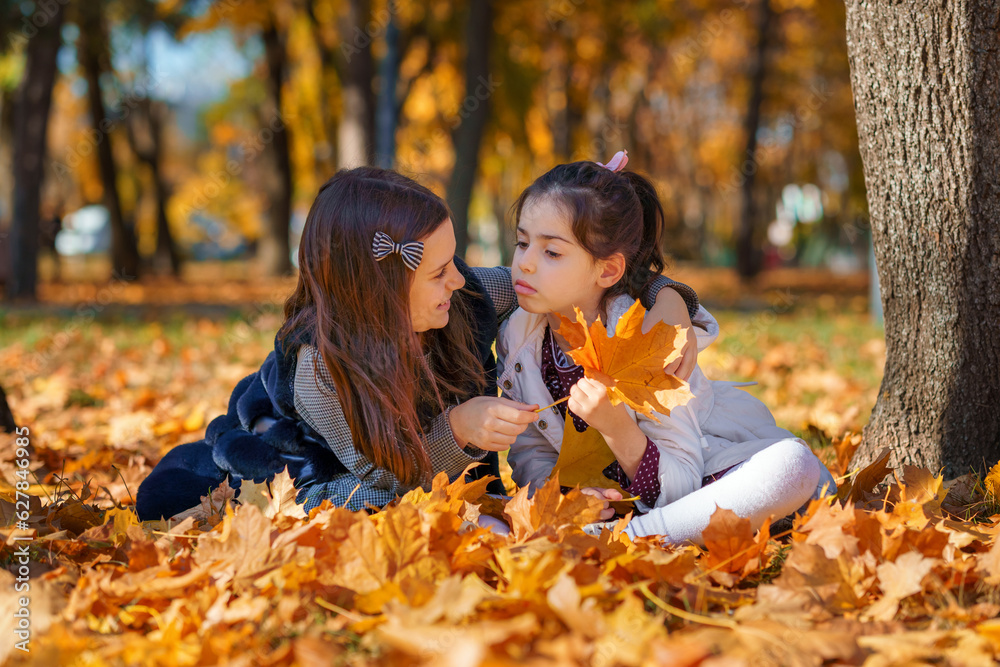 two girls are sitting in a glade of yellow maple leaves in an autumn city park, children are playing and enjoying, picking leaves near a tree, beautiful nature, bright sunny day two girls are sitting in a glade of yellow maple leaves in an autumn city park, children are playing and enjoying, picking leaves near a tree, beautiful nature, bright sunny day