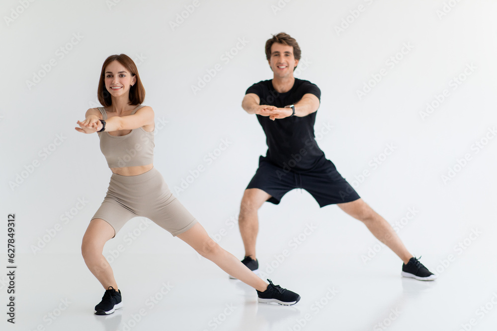 Obraz premium Cheerful young caucasian guy and lady in sportswear enjoy training for legs together, fit in gym