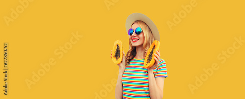Summer portrait of happy cheerful young woman having fun with fresh papaya fruits wearing straw hat  sunglasses on yellow background