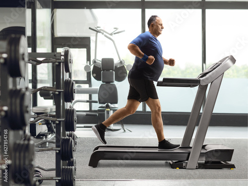 Full length profile shot of a mature man running on a treadmill at a gym