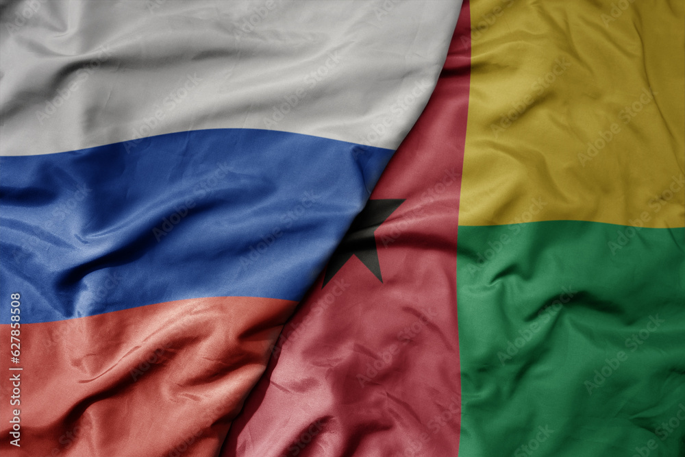 big waving realistic national colorful flag of russia and national flag of guinea bissau .