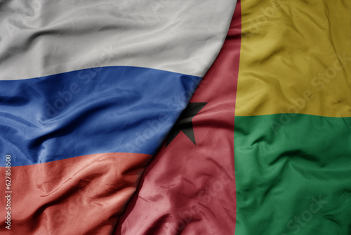 big waving realistic national colorful flag of russia and national flag of guinea bissau .