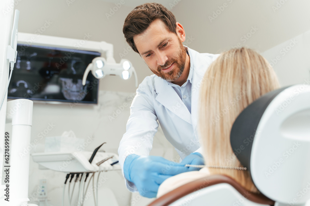 Obraz premium Portrait of handsome middle aged dentist consulting female patient with blond hair, in dental chair