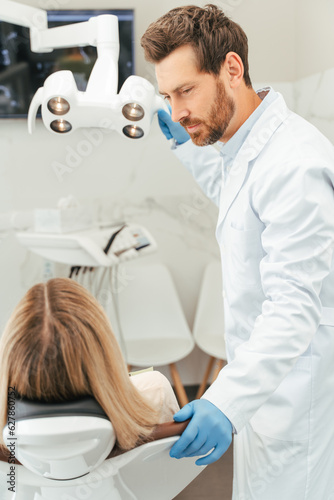 Portrait of middle aged dentist consulting female patient with blond hair, sitting in dental chair