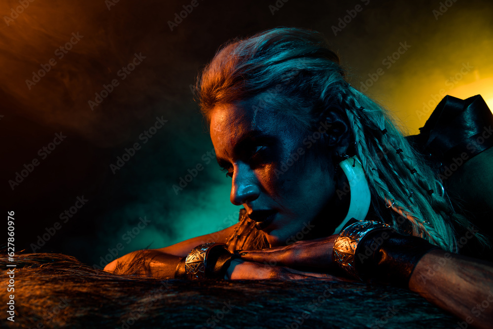 Photo of mysterious creepy viking savage girl bloody body art animal fur blue yellow lights isolated on dark background