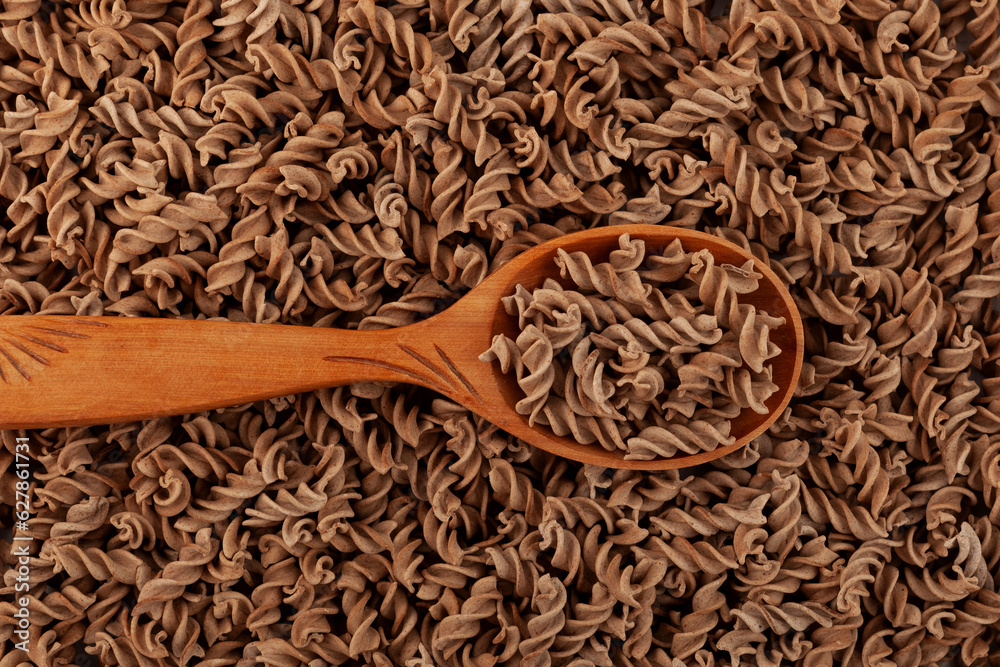 Gluten free flax pasta in wooden spoon. Uncooked Fusilli made of flaxseed flour, closeup. Pasta
