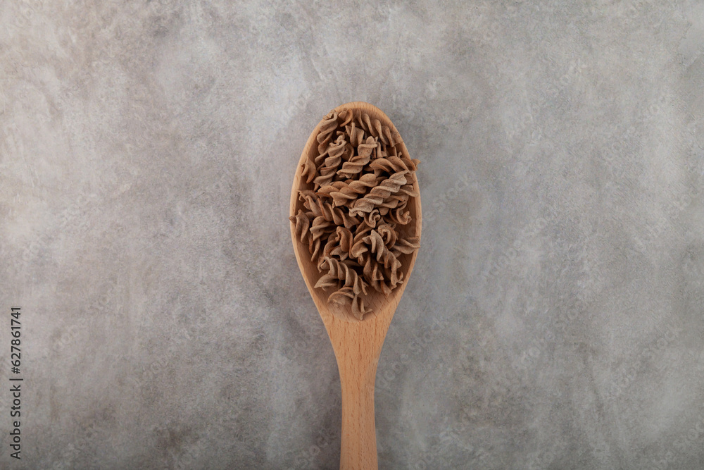 Gluten free flax pasta in wooden spoon on grey background, top view