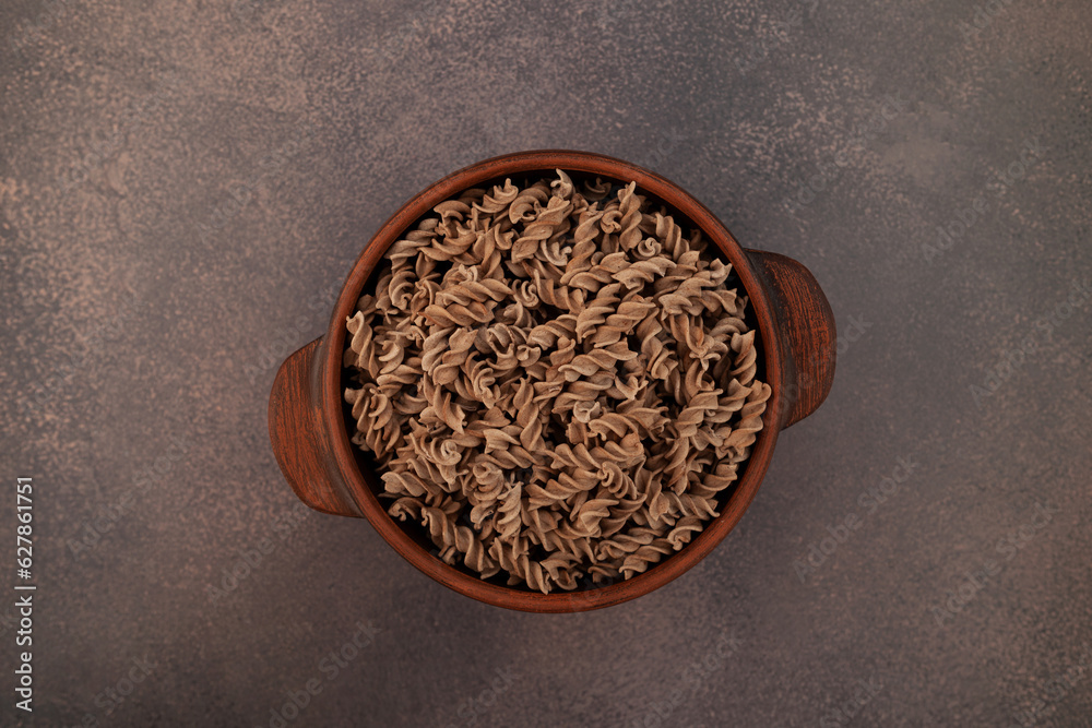 Uncooked Fusilli made of flaxseed flour in clay bowl on brown background, top view. Pasta di