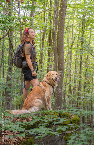 girl hiker smiling with her golden retriever dog observes nature in forest