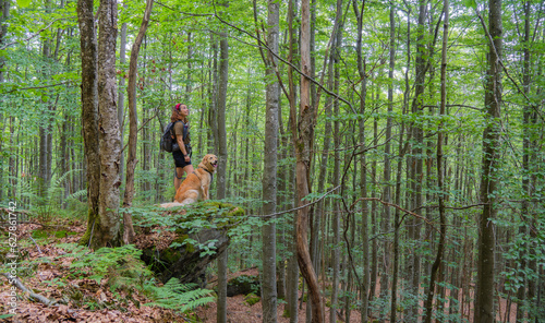 girl hiker smiling with her golden retriever dog observes nature in forest