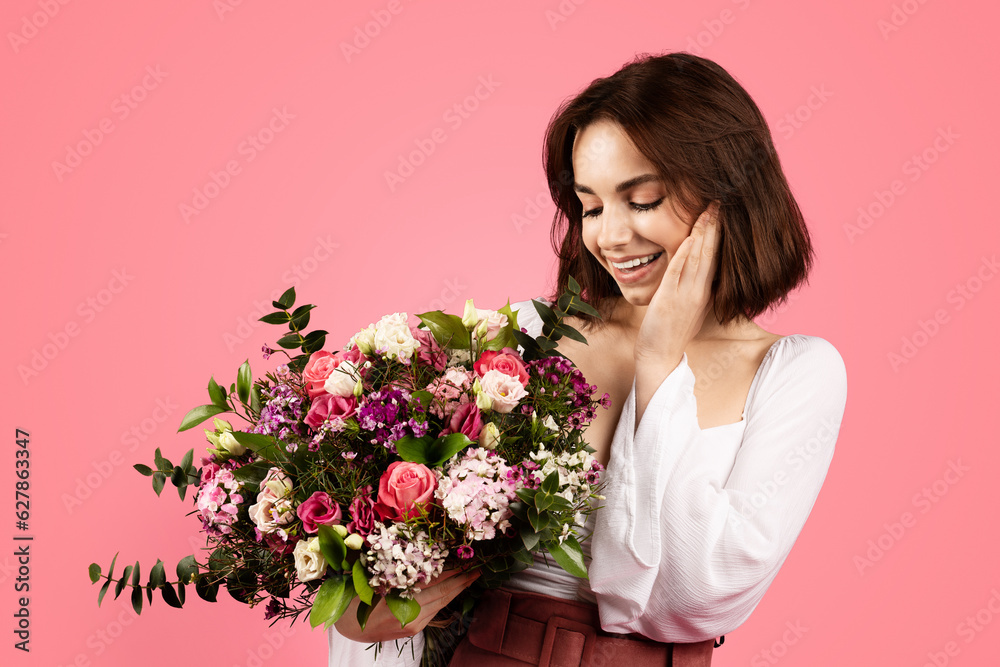 Happy millennial caucasian brunette woman enjoy bouquet of flowers, isolated on pink background Happy millennial caucasian brunette woman enjoy bouquet of flowers, isolated on pink background