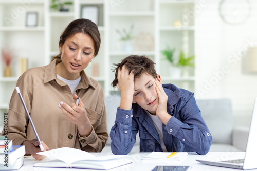 Cute and boring study at home, mom explains homework to son, family study at home sitting in living room, son doesn't understand homework upset and bored. photo