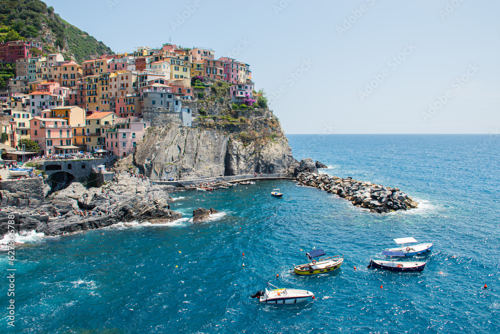 Colourful buildings on a cliff and boats on the water in the foreground in Cinque Terre, Italy.