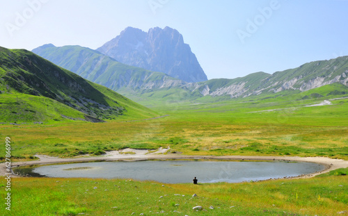 paesaggio idilliaco di montagna con lago e persona isolata seduta a meditare © Michele