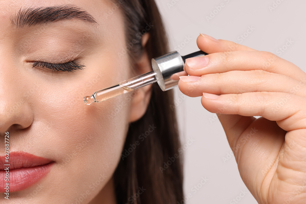 Young woman applying essential oil onto face on light grey background, closeup Young woman applying essential oil onto face on light grey background, closeup