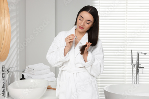 Young woman applying essential oil onto hair in bathroom