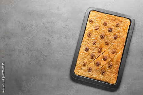 Delicious baklava with walnuts in baking pan on grey textured table, top view. Space for text