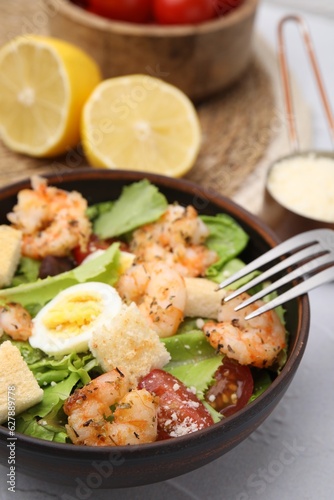 Delicious Caesar salad with shrimps and fork served on white table