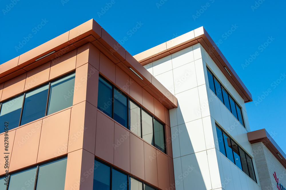 The roofs of a modern commercial building under blue sky and white clouds. The exterior of the new building is rusty, orange, and cream in color metal composite panels with black glass windows. 