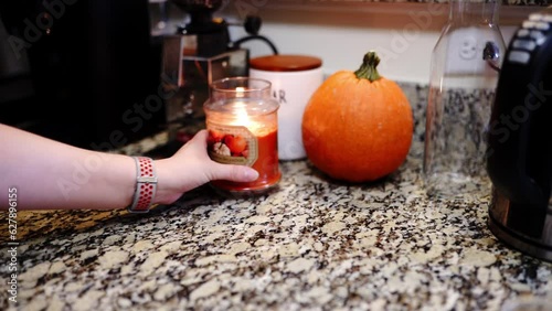 Hand of woman moves candle closer to the pumpkin.  Hand placing white cup on table. 