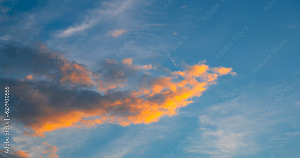 SUNSET CLOUDS with White airliner transports passengers while it pulling white contrails in dark blue cloudy sky.