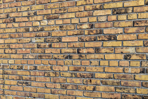 Full frame texture background of a shabby chic old mottled yellow and brown color exterior brick wall, with weathered bricks in a common bond brickwork pattern (angle view)