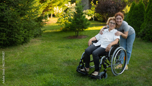 Caucasian woman hugging an elderly mother sitting in a wheelchair. Walk outdoors. 