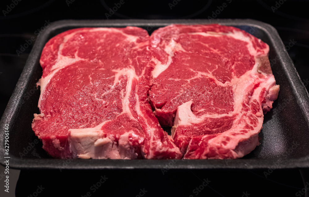 Beef steak. Fresh raw beef steak isolated on black background, top view. Raw rib eye steaks on styrofoam tray. Marbled beef raw meat steak. Nobody, selective focus